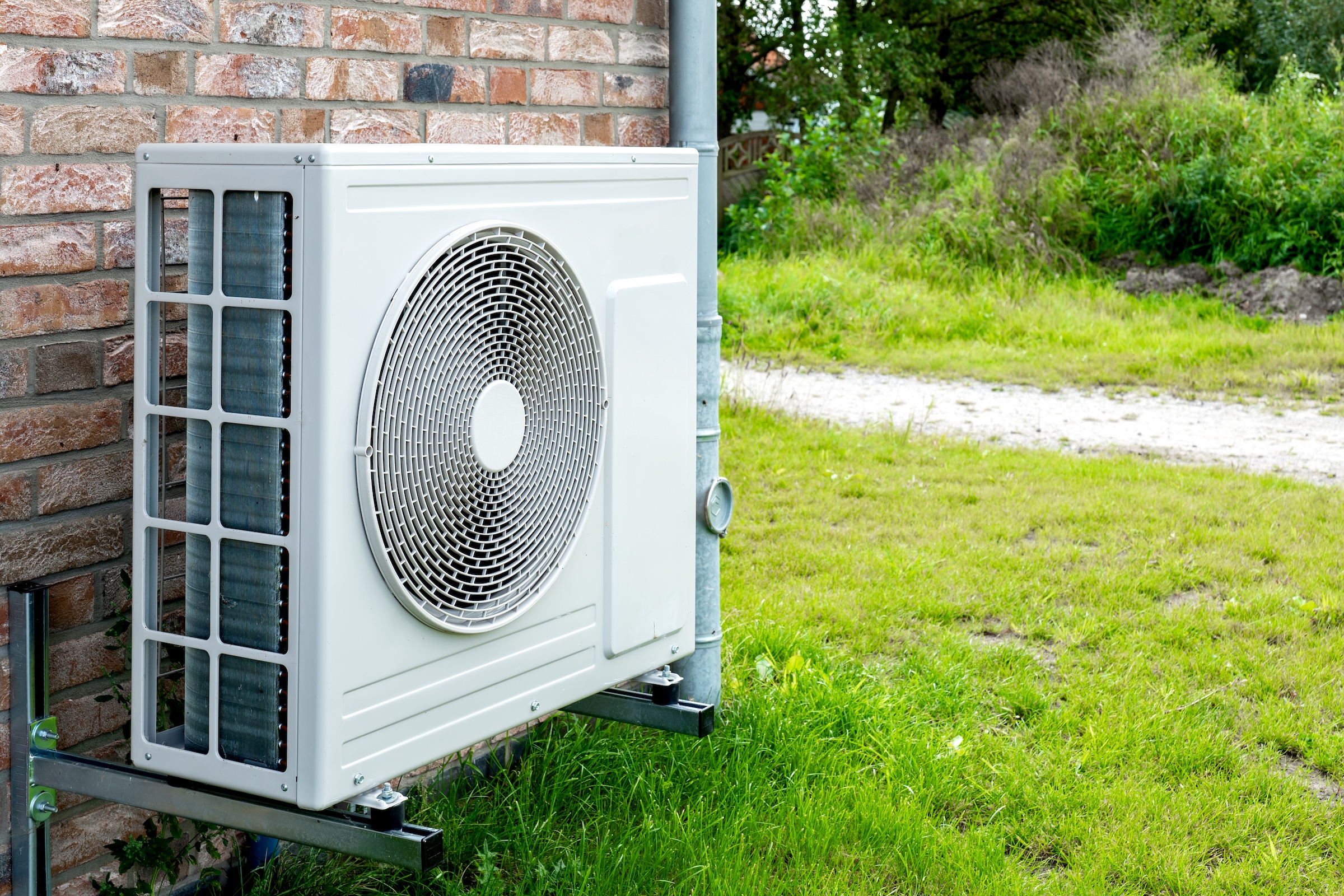A heatpump sits on brackets against the brick wall of a home.